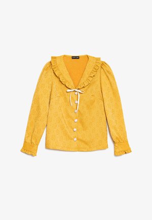 Κίτρινο μπλούζα με μακριά μανίκια και υφή με λουλούδια, ρεβέρ με βολάν και μανσέτες, λευκά κουμπιά από μαργαριτάρι και λευκό κορδόνι στον λαιμό.