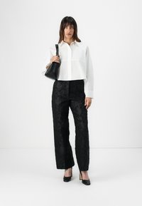White cropped shirt with a collar, black textured wide-leg pants with floral patterns, and black pointed-toe heels. Small black shoulder bag.