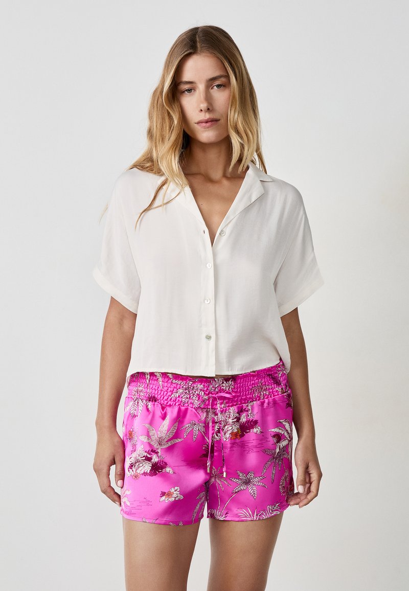Witte kortekleurige overhemd met knopen, gecombineerd met roze shorts met bloemenpatroon, voorzien van een elastische tailleband en trekkoord. Smooie stofstructuur.