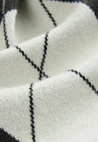 Tkanina z mieszanki wełny o kremowej bazie z czarnym wzorem w diamenty, miękką teksturą i lekko puszystym wykończeniem.