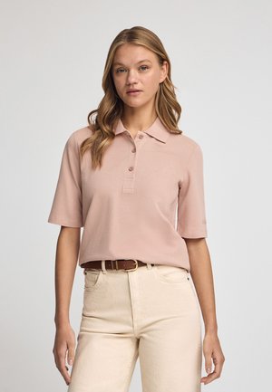 Polo shirt rosa chiaro con colletto, maniche corte e patta con tre bottoni. Indossato con jeans a vita alta beige e una cintura marrone.