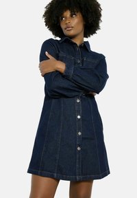 Donkerdenim shirtjurk met een knoopsluiting aan de voorkant, lange mouwen en een getailleerde taille, met een lichte uitlopendheid aan de zoom en contrasterende stiksels.