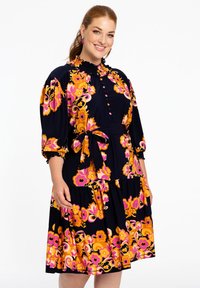 Blumenkleid mit navy Grundfarbe, das lebhafte orange und rosa Blumen trägt. Es hat einen Rüschensaum, eine Knopfleiste und eine Taillierung mit Gürtel.