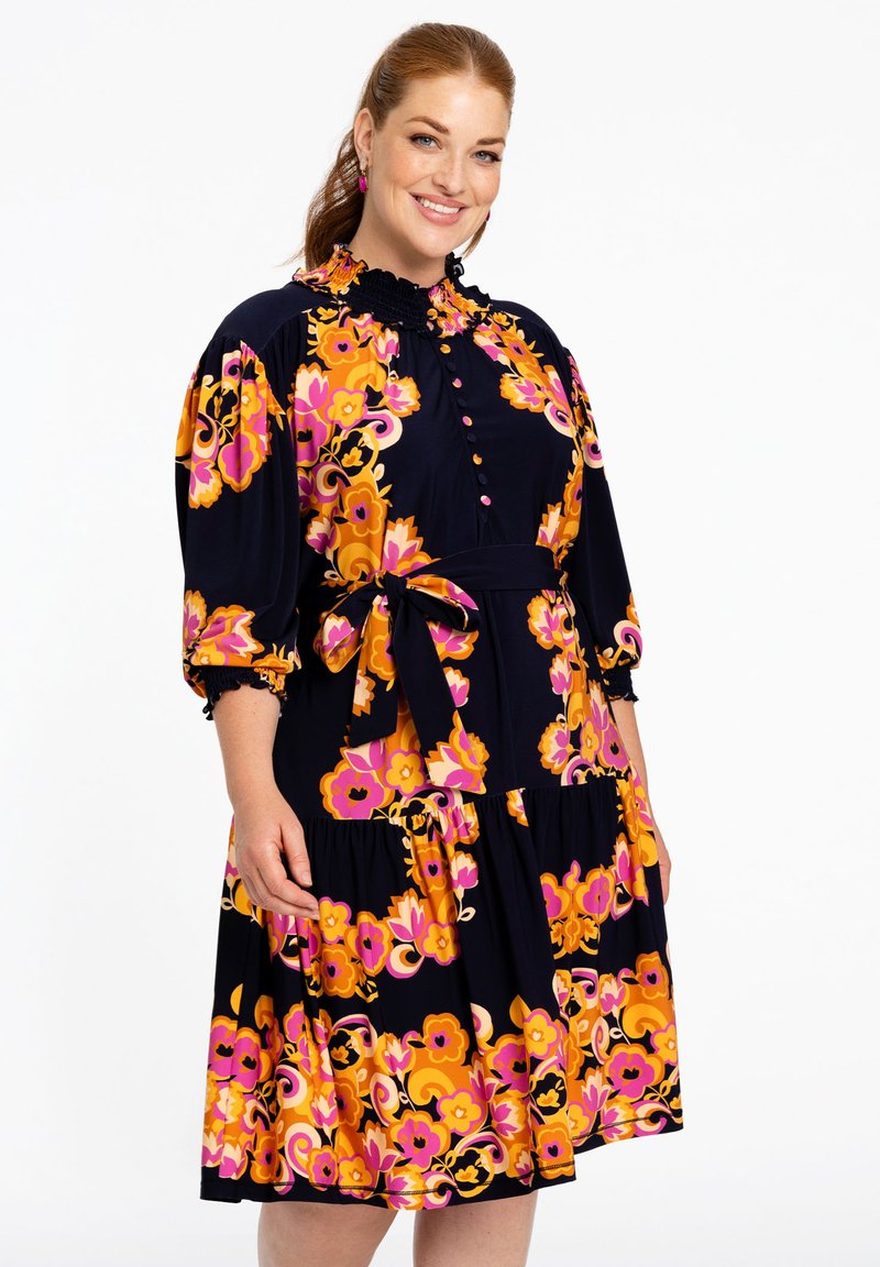 Blumenkleid mit navy Grundfarbe, das lebhafte orange und rosa Blumen trägt. Es hat einen Rüschensaum, eine Knopfleiste und eine Taillierung mit Gürtel.