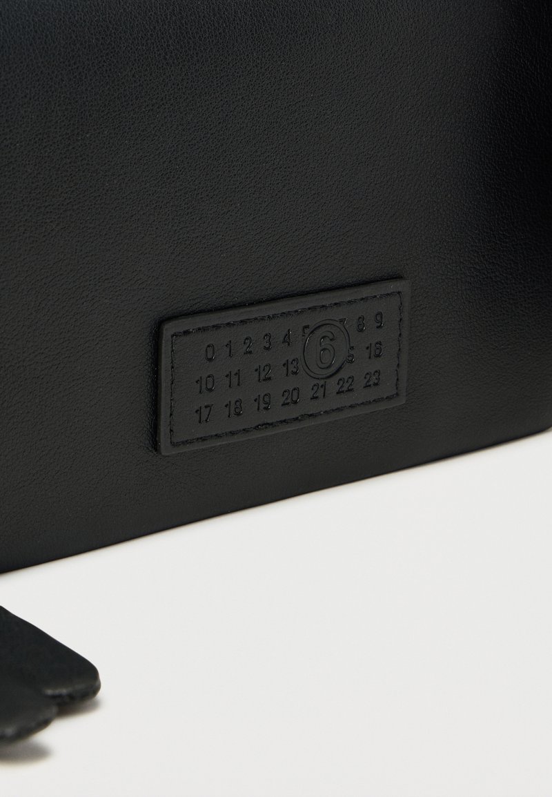 Article en cuir noir avec une pièce rectangulaire cousue affichant les chiffres de 0 à 23, avec le chiffre 6 encerclé au centre.