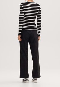 Czarny i biały prążkowany top z długimi rękawami, zestawiony z luźnymi czarnymi spodniami oraz białymi sneakersami z czarnymi detalami.