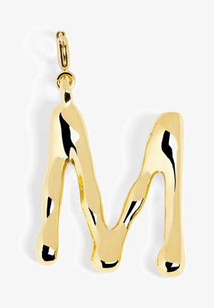 Colgante de oro con forma de la letra "M". Presenta un diseño fluido y orgánico con un acabado pulido y un pequeño lazo para su sujeción.