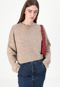 Strickpullover mit lockerer Passform, der pastellfarbige Streifen auf einem neutralen Hintergrund zeigt, kombiniert mit einem rockigen Jeansrock und einem roten Schulterstrap.