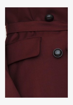 Cappotto in tessuto bordeaux con colletto a punta, grandi bottoni neri e cintura in vita. Presenta una tasca laterale e una texture liscia.
