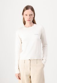 Maglione color crema realizzato in morbido punto con collo e polsini a coste. Presenta un delicato logo ricamato sul petto.