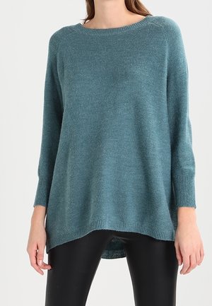 Maglione oversize teal con scollo rotondo, polsini a costine e un orlo posteriore più lungo. Realizzato in un morbido materiale knit con una texture liscia.