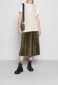 Krämfärgad ribbade väst med knappar, vit t-shirt, olivgrön plisserad kjol, svarta chunky ankelskor och en leopardmönstrad väska.