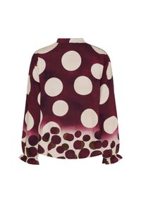 Blus med långa ärmar och stora krämfärgade prickar mot en burgundyröd bakgrund, som övergår till mindre bruna och burgundyröda prickar vid fållen och ärmsluten.