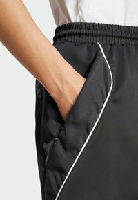 Sorte treningsshorts med en glatt tekstur, med hvit pipingdetalj langs siden og en hånd i sidelomma.