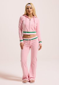 Haut de hoodie court rose avec des rayures vertes et blanches, associé à un pantalon évasé rose. Le matériau semble doux, avec une texture lisse et une coupe relaxante.
