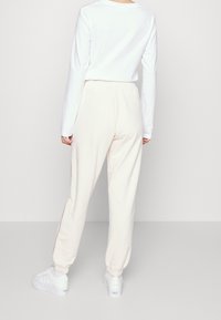 Vit långärmad skjorta i kombination med krämfärgade sweatpants med elastiska ärmslut och sidostricka, kompletterat med vita sneakers.