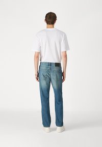 Relaxed-fit jeans voor heren in lichtblauwe denim met achterzakken en een zwart logo-label. Gecombineerd met een eenvoudig wit T-shirt en sneakers.