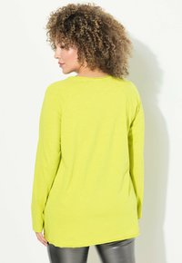 Maglietta a maniche lunghe di un vivace giallo, realizzata in tessuto morbido, con scollo rotondo e maniche raglan. L'orlo è leggermente più lungo sul retro.