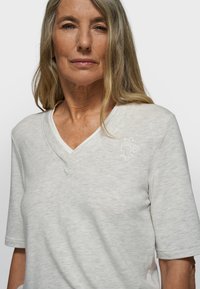 T-shirt gris clair à col en V en tissu doux, avec manches courtes et un détail de logo brodé sur la poitrine.