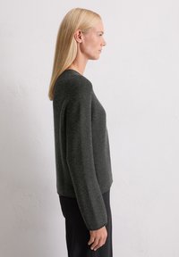 Dunkelgrauer, strukturierter Strickpullover mit Rundhalsausschnitt und langen Ärmeln, kombiniert mit schwarzen, vertikal gestreiften Hosen. Seitenansicht, die die Passform zeigt.