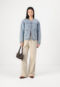 Svetlo modra jeans jakna z okroglim ovratnikom, zapenjanjem na gumb in dvema sprednjima žepoma. V paru s bež širokimi hlačami in temno torbico.