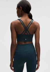 Urheilurintaliivit tummansinisellä sävyllä, joissa ristikkäiset hihnat selkäpuolella ja teksturoitu pinta, yhdistettynä samanvärisiin korkeavyötäröisiin leggingseihin.