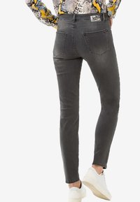 Jeans ajustados grises con un acabado ligeramente desgastado, que cuentan con dos bolsillos traseros y una etiqueta de marca en la cintura. Combinados con zapatillas blancas.