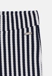 Stripete leggings i marineblått og hvitt, med teksturert stoff og et sølvfarget merkeakcent. Loddrette striper skaper et distinkt mønster.