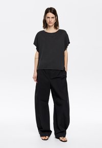 Zwart T-shirt met korte mouwen en ronde halslijn, versierd met strass-steentjes aan de voorkant, gecombineerd met losse zwarte broek en slippers.