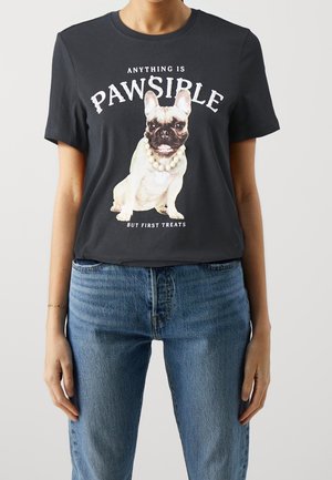 Osoba w czarnej koszulce z buldożkiem francuskim w naszyjniku z pereł i napisem "Wszystko jest możliwe, ale najpierw przysmaki."