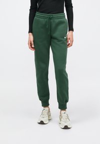 Zaļas kokvilnas sporta bikses ar elastīgu aukliņu jostu un ribotu apmali, uz kreisā augšstilba mazs balts Nike logotips.