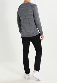 Grå långärmad tröja med rundad halsringning, kombinerad med svarta byxor och vita sneakers. Texturerad yta och avslappnad passform.