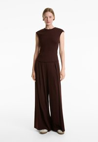 Top senza maniche color mogano con una silhouette aderente, abbinato a pantaloni a gamba larga dello stesso colore. Tessuto morbido e strutturato con cuciture minime.