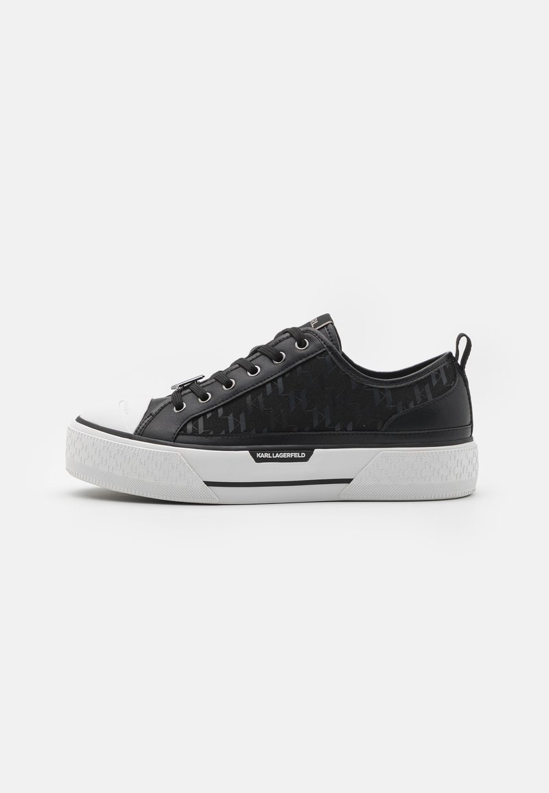 Schwarze Low-Top-Sneaker mit gemustertem Canvas-Obermaterial, weißer Gummikappe, strukturiertem Sohlenprofil und Logo-Akzent an der Seite. Metallösen für die Schnürsenkel.
