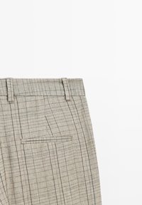 Pantalon beige à carreaux avec passants de ceinture et une poche arrière passepoilée unique, présenté à plat sur un fond blanc.