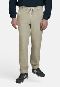 Beige broek met een textuurafwerking, voorzien van een trekkoord in de taille. Gecombineerd met donkergrijze sneakers met witte accenten.