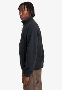 Fleece jacket in dark navy with a high collar, zippered pockets, and contrasting black panels, featuring a soft, textured fabric.
