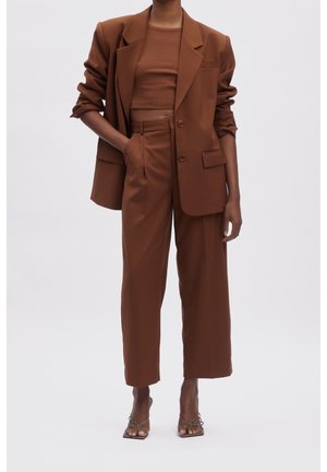 Femme portant un pantalon large marron raccourci, un blazer assorti aux manches retroussées, un haut ajusté et des sandales à talons ouvertes.