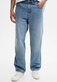 Světle modré džíny z denimu s volným střihem, pětikapsovým designem, dvojitým prošitím a ohrnutými lemy. Nošeny s bílými teniskami.