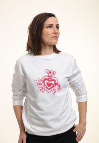 Sudadera blanca con un gran gráfico rosa de tres personajes de dibujos animados rodeados por un diseño de corazón, con detalles texturizados.