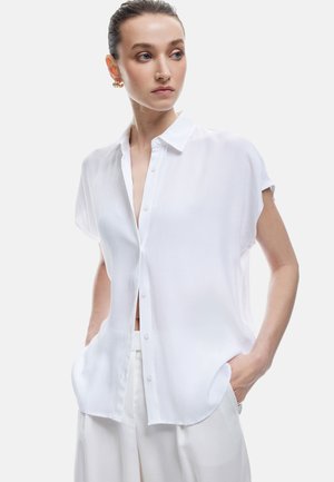 Camicia bianca a maniche corte con bottoni e vestibilità rilassata, dotata di colletto e tasche laterali, realizzata in tessuto leggero e testurizzato.