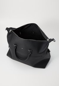 Sac en cuir noir avec un extérieur texturé, quincaillerie en argent, fermeture éclair et ouverture sur le dessus, révélant un intérieur spacieux.