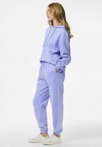 Ljubičasta majica s kapuljačom i odgovarajuće trenirka od mekog tkanja. Majica ima vezice; trenirka ima elastične manžete i bočne džepove.