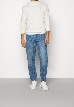 Ljusbeige tröja kombinerad med ljusblå mönstrade jeans. Vita sneakers kompletterar looken. Jeansen har en strukturerad prickig design.