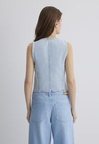Ärmellose Jeansweste in Hellblau mit hohem Kragen und verkürztem Design. Sichtbare Nähte und ein Etikett am Taillenbund.
