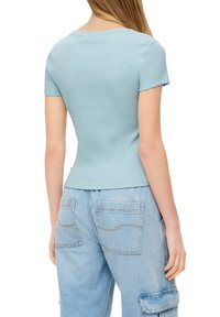 Lichtblauwe rib gebreide top met korte mouwen en een ronde hals. Heeft onafgewerkte zoomranden. Gedirigeerd met lichtblauwe baggy jeans met twee achterzakken.