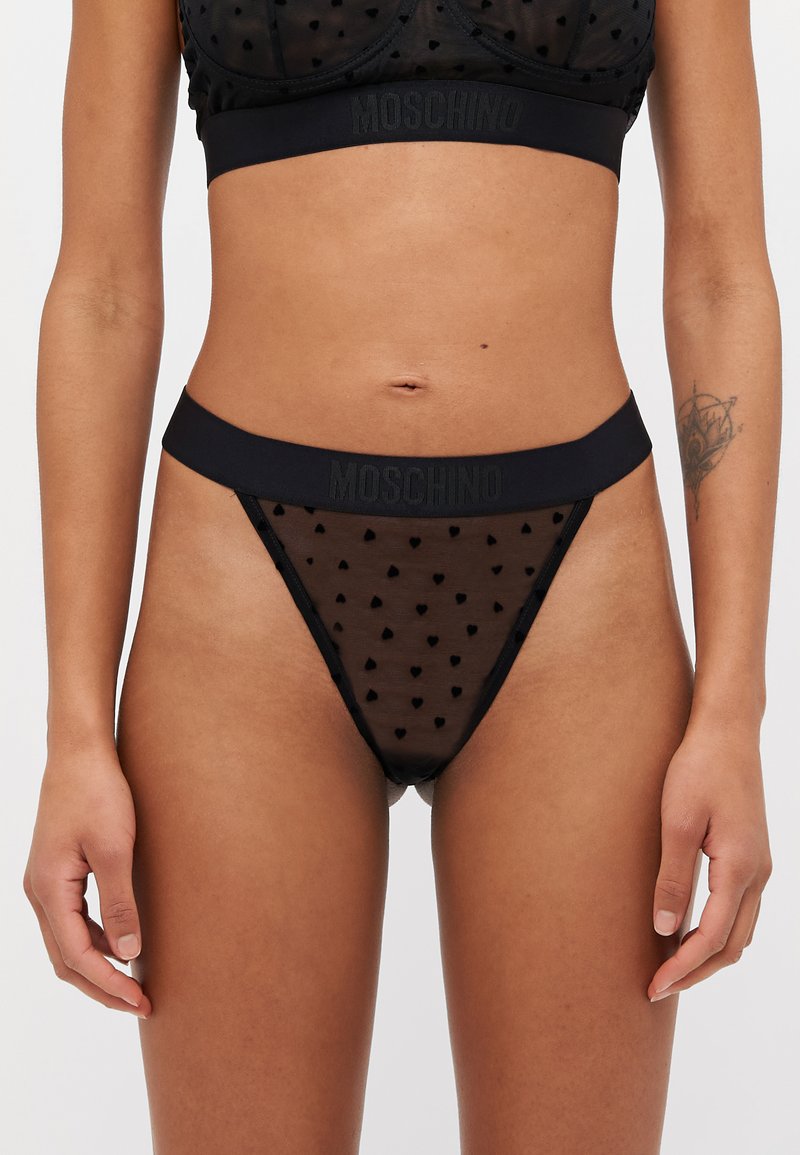 Zwarte mesh ondergoed met hartpatronen en een vaste tailleband met het "Moschino"-logo. De textuurstof voegt visuele interesse toe.