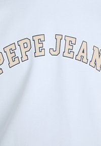Camiseta de algodón azul claro con un estampado de texto curvado en beige que dice "PEPE JEANS". Textura suave y diseño casual.