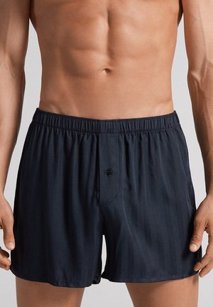 Námořnické modré pletené trenky s elastickým pasem, s jedním knoflíkem na zapínání a jemnými vertikálními pruhy.