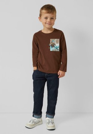 Braunes Langarmshirt mit Rundhalsausschnitt und grafischem Print. Kombiniert mit dunkelblauen Jeans und weißen Sneakers mit grauen Akzenten.